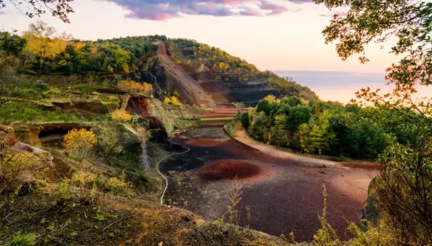 Paisaje del parc natural de la zona volcànica de la Garrotxa con laderas escalonadas, vegetación otoñal y el cielo rosado del atardecer.
