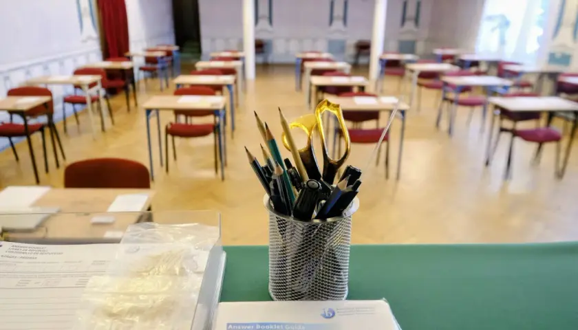 Przygotowania do matury z angielskiego: ołówki, nożyczki i zeszyty czekają na uczniów w pustej sali egzaminacyjnej.