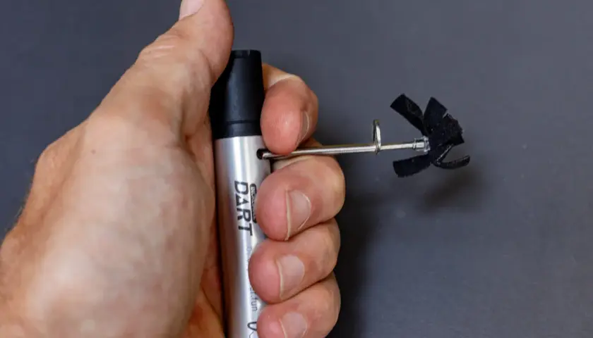 A hand holds a silver "DART" marker with a small, black, propeller-like attachment. This is part of a stans dart review.