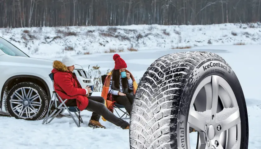 Ett par njuter av en paus i snön bredvid en bil, med en vinterdäck i förgrunden. Välj dubb eller dubbfritt för din trygghet.