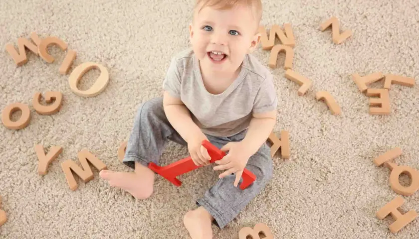 Bambino sorridente circondato da lettere di legno, un modo divertente per iniziare a capire come sviluppare il linguaggio nei bambini.