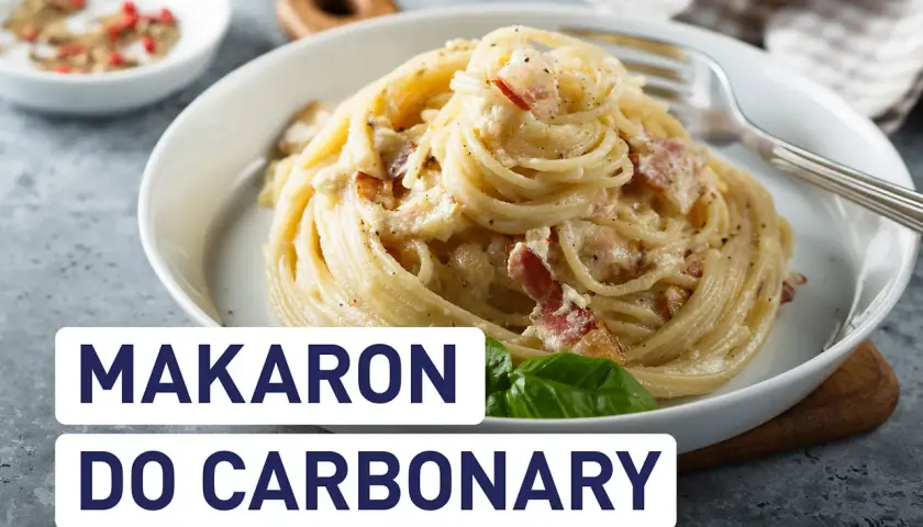 Pyszny makaron do carbonary z boczkiem i kremowym sosem, podany w białej misce. Obok przyprawy i liść bazylii.