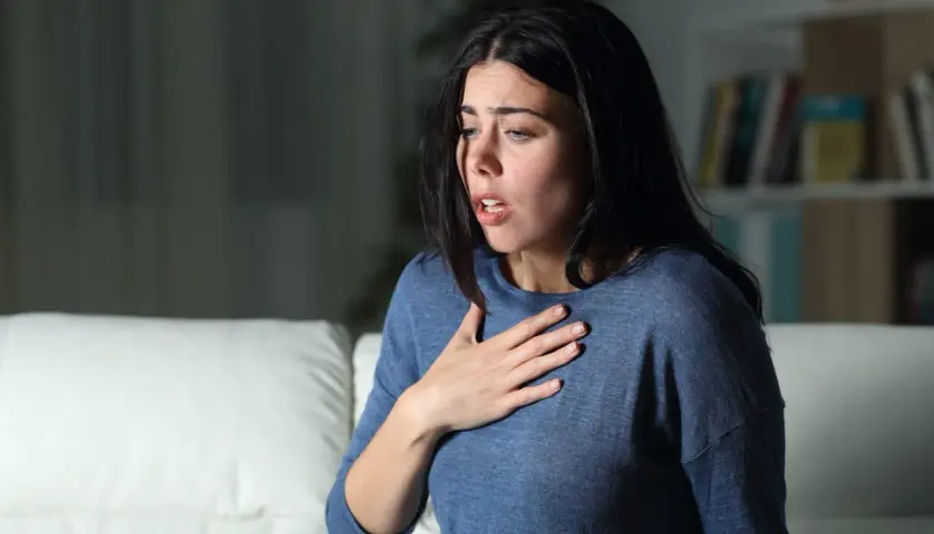 Donna con mano sul petto, respiro affannoso, espressione di chi soffre di attacchi di ansia.