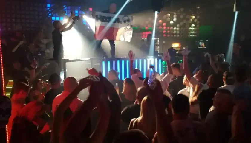 Tłum na parkiecie klubu, DJ na scenie z flagą Polski, światła i energia prawdziwego rave.