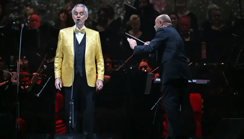 Andrea Bocelli w Polsce, w złotym fraku, śpiewa pod batutą dyrygenta.