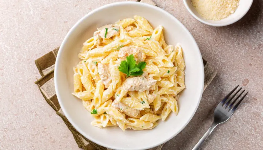 Penne w kremowym sosie, przypominające fettuccine alfredo, z kawałkami kurczaka i natką pietruszki.