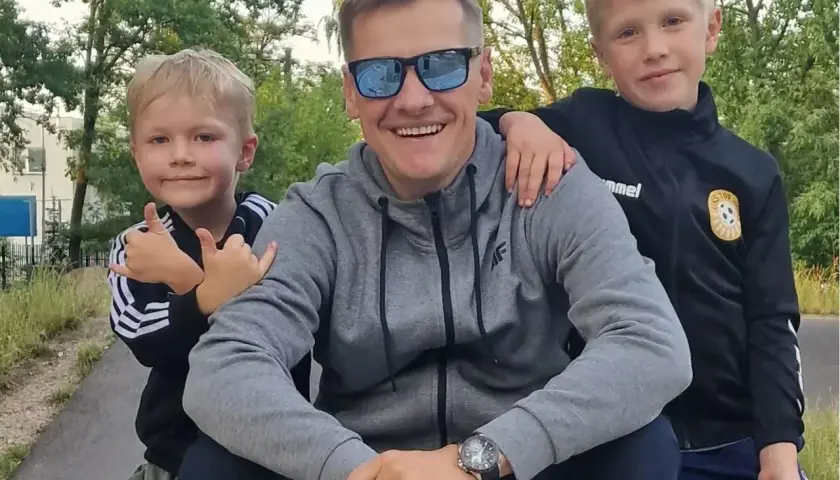 Marcin Mroczek z uśmiechem i dwoma synami, którzy przytulają się do niego.