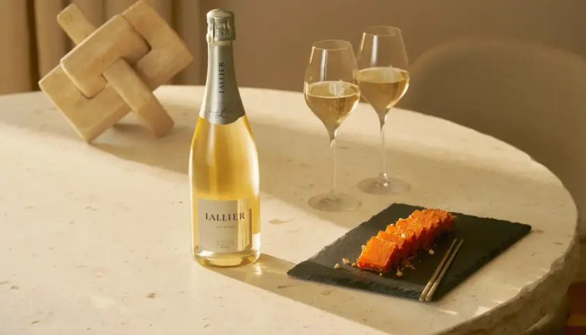 LALLIER Blanc de Blancs Champagner mit zwei Gläsern und einem Holzpuzzle.