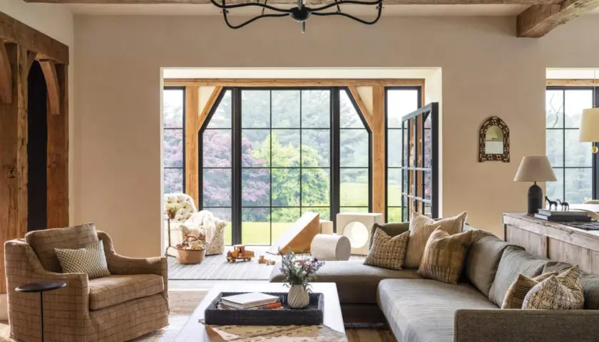 A cozy living room with exposed wooden beams, a large sectional sofa, and a plaid armchair, embodying rustic chic interior design.