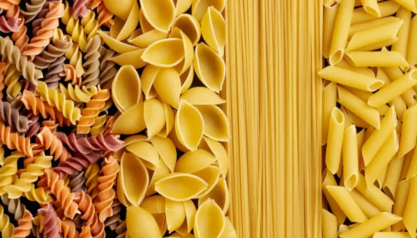 Różne rodzaje makaronu: kolorowe fusilli, muszelki, spaghetti i penne. Wybór wpływa na indeks glikemiczny posiłku.