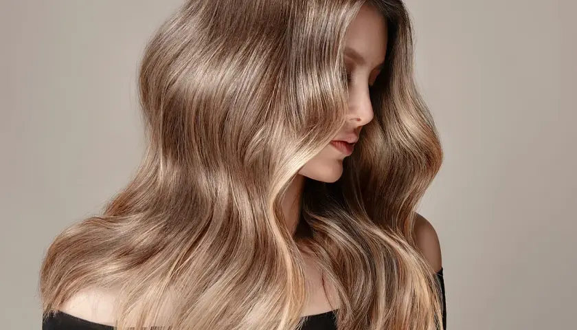 Mujer con cabello largo y ondulado en tonos castaños y rubios, ideal para quienes buscan cómo quitar el tinte del cabello y dejarlo natural.