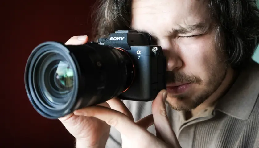 Mężczyzna zamyka oko, patrząc przez wizjer aparatu Sony Alpha 7. Premiera Sony a7 IV budzi emocje.