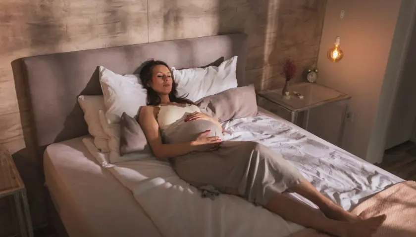 Femme enceinte se repose sur le dos, ventre arrondi, dans une position confortable pour dormir enceinte 1er trimestre.