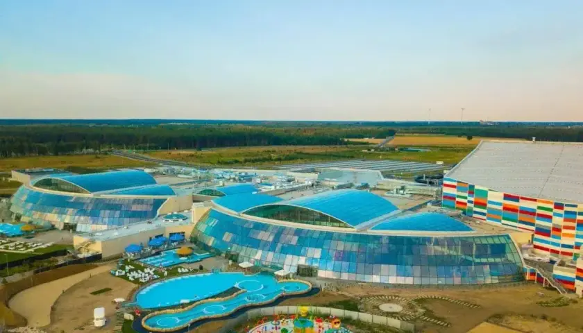Nowoczesny park wodny Suntago z przeszklonymi dachami i kolorową fasadą, otoczony zielenią.
