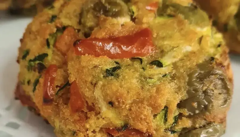 Polpette di zucchine dorate e saporite, con pomodorini e olive verdi, pronte per essere gustate.