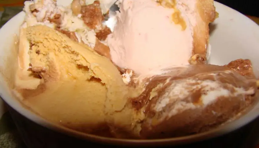 Un tazón lleno de helado de leche cremoso, con sabores de caramelo, fresa y chocolate, adornado con trozos de galleta.