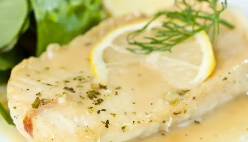 Filete de pescado bañado en una deliciosa salsa de limón para pescado, adornado con una rodaja de limón y eneldo.
