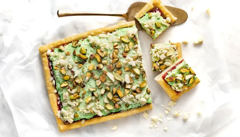 Ciasto z zieloną masą pistacjową i posiekanymi pistacjami, pokrojone na kwadraty.