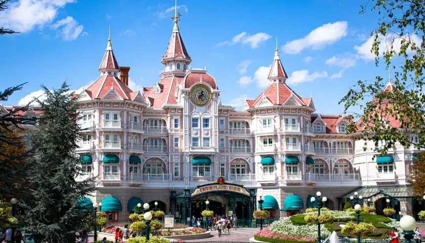 Grand hôtel rose de style victorien avec des tours, un grand cadran d'horloge et des jardins fleuris.