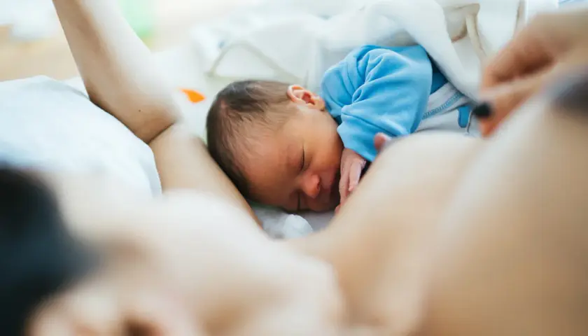 Malutki noworodek śpi wtulony w mamę. Jego brzuszek jest taki okrągły i słodki, jak u każdego niemowlaka.