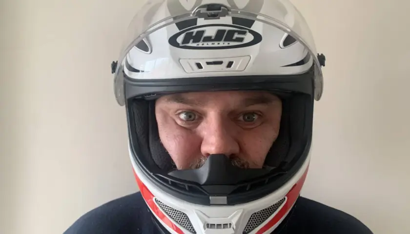 Hombre con casco de moto HJC blanco y rojo, listo para elegir su próxima aventura.