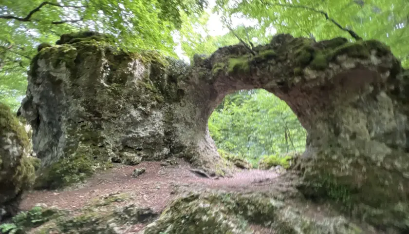 Arco natural cubierto de musgo en la sierra de Entzia, rodeado de árboles frondosos.