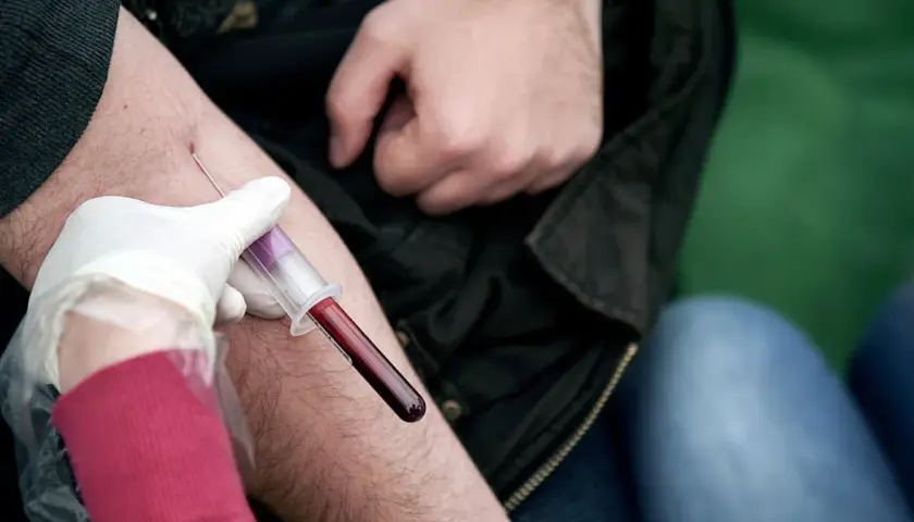 Pobieranie krwi do badania. Lekarz w białej rękawiczce pobiera krew do probówki, sugerując, że **ALT AST podwyższone** może być przyczyną.