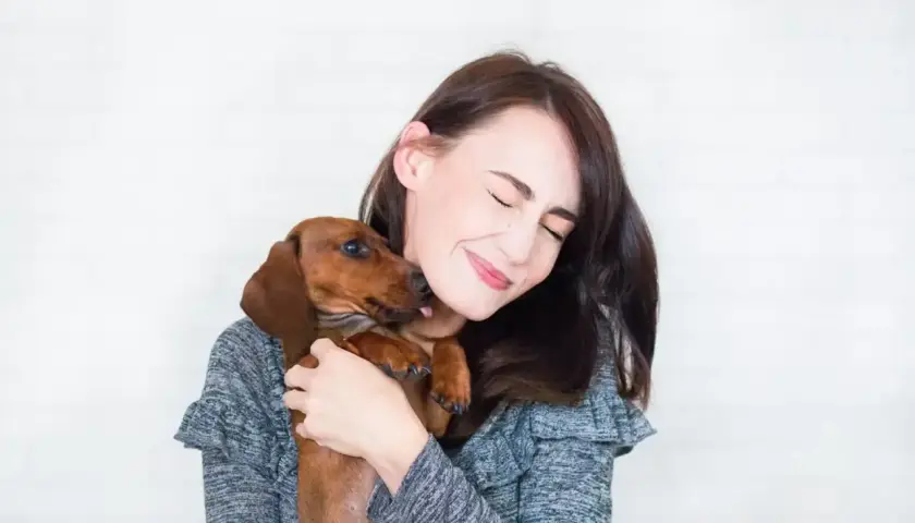 Un perro salchicha le lame la cara a su dueña, que sonríe con los ojos cerrados. Es la prueba de que mi perro me sigue a todas partes.