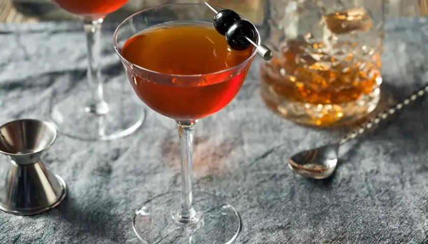 Cocktail au whisky garni de cerises, servi avec un verre de whisky et un jigger. Le whisky est-il bon pour les artères ? Une question à méditer.