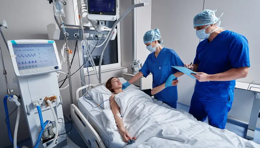 Médicos monitorean a paciente en UCI. Una enfermera ajusta el flequillo cortina de la joven mientras un doctor anota datos.