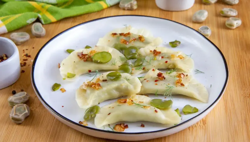 Pyszne pierogi z bobem, posypane skwarkami i koperkiem, prezentują się apetycznie na talerzu.