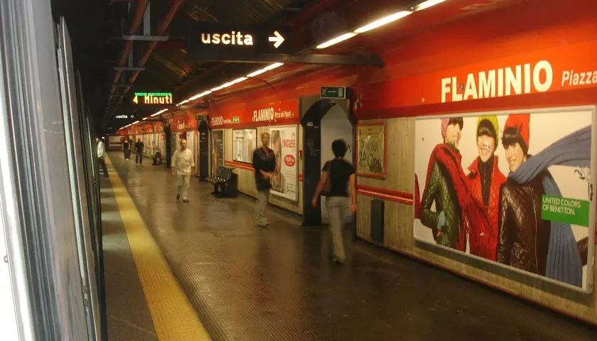 Stazione della metro Roma Nord, banchina con persone in attesa, cartelloni pubblicitari e indicazioni per l'uscita.