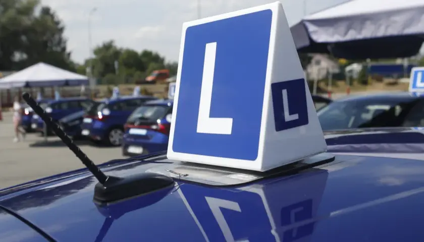 Niebieskie samochody z literą "L" na dachu, symbolizujące naukę jazdy i zasady egzaminu na prawo jazdy.
