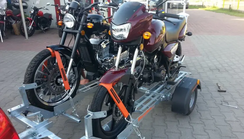 Dwa motocykle na przyczepie, zabezpieczone pasami.