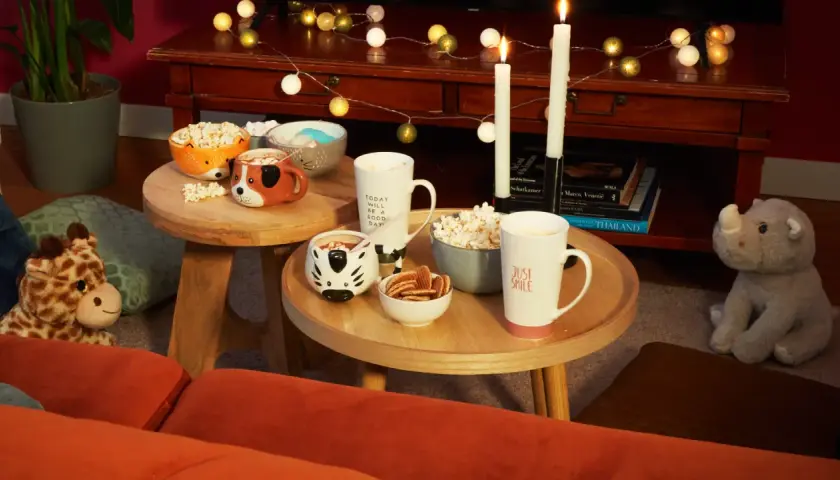 Tavolini bassi con tazze a tema animale, popcorn e biscotti, perfetti per una serata cinema a casa.