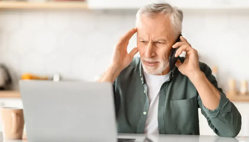 Zmartwiony mężczyzna rozmawia przez telefon, trzymając się za głowę. Może szuka siła wyższa powody problemów z laptopem.