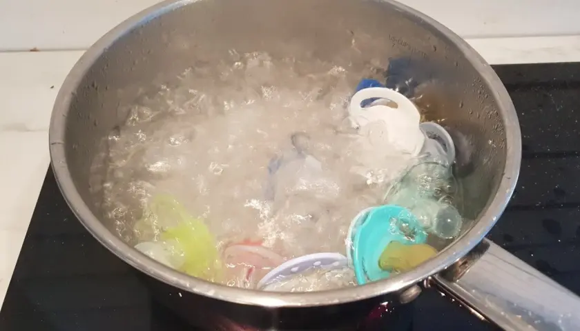 Flera färgglada nappar ligger i en kastrull med kokande vatten. Det är dags att koka nappar för hygien.