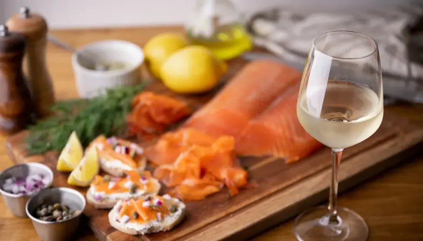 Un verre de vin blanc frais accompagne un saumon fumé et des toasts. Parfait pour savoir quel vin avec du saumon en papillote.