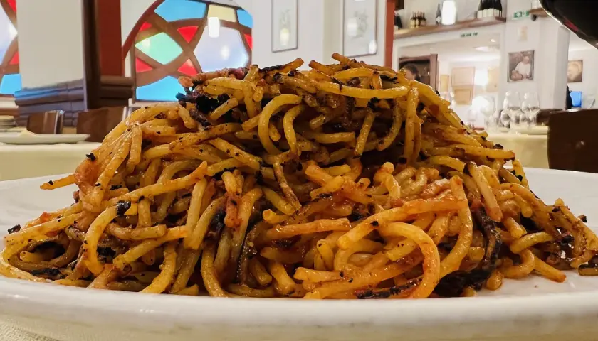 Un piatto di spaghetti con pomodoro e basilico, un classico su cosa mangiare a Bari. Il tutto servito in un ristorante con vetrate colorate.