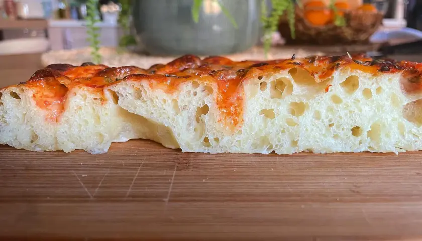 Fetta di focaccia soffice e alveolata, con pomodoro e formaggio filante. Perfetta per uno spuntino o un pasto veloce.