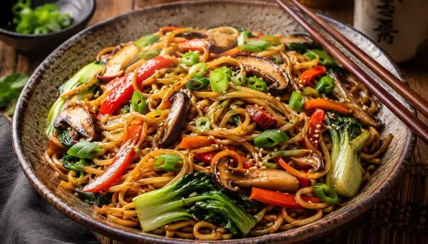 Pyszny makaron chiński z warzywami: grzybami shiitake, papryką, marchewką i pak choi, posypany szczypiorkiem i sezamem.