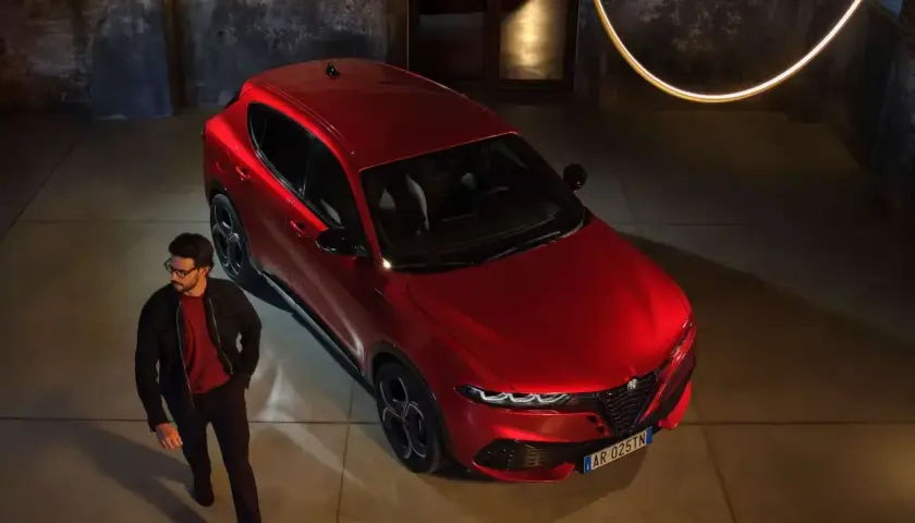Elegancki mężczyzna obok czerwonego Alfa Romeo Tonale. Sprawdź aktualną alfa romeo tonale cena i odkryj jego styl.
