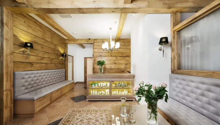 Wnętrze spa z drewnianymi elementami, kanapami, ladą z kosmetykami i bukietem róż.