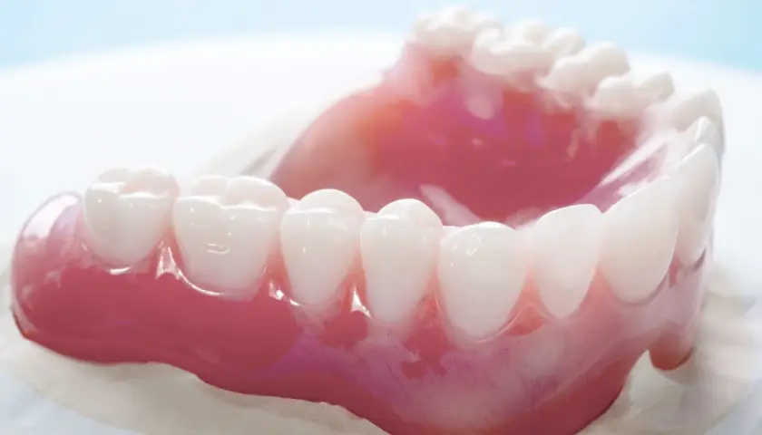 Un primo piano di una dentiera rosa con denti bianchi. La dentiera mi fa vomitare.