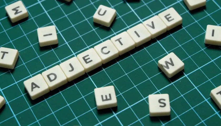 Tessere con lettere formano "ADJECTIVE". Alcune lettere sparse, come "S", suggeriscono la creazione di aggettivi con s.