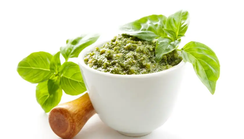 Aksamitne, zielone pesto w białej miseczce, ozdobione listkami bazylii. Obok drewniany tłuczek. To najlepsze pesto, jakie możesz sobie wyobrazić!