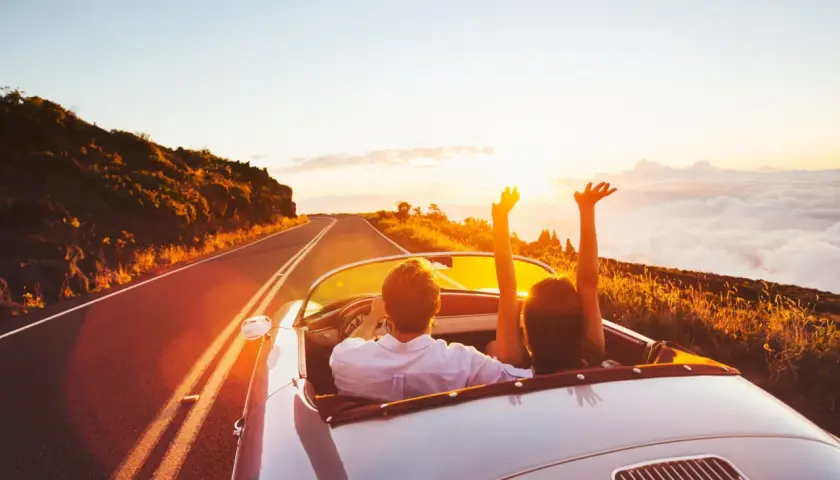 Coppia in auto decappottabile al tramonto, con le braccia alzate, godendosi un itinerario Croazia da sogno.