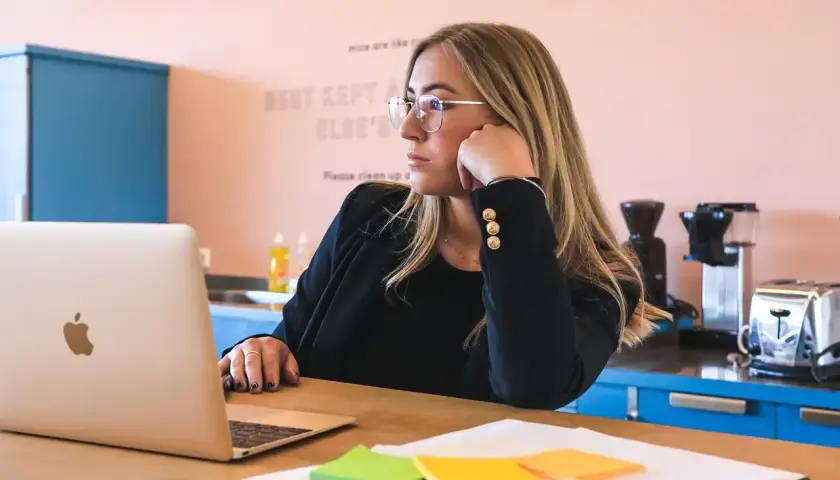 Kobieta w okularach zastanawia się, ile trwa staż z urzędu pracy, patrząc na laptopa. Na biurku kolorowe karteczki.