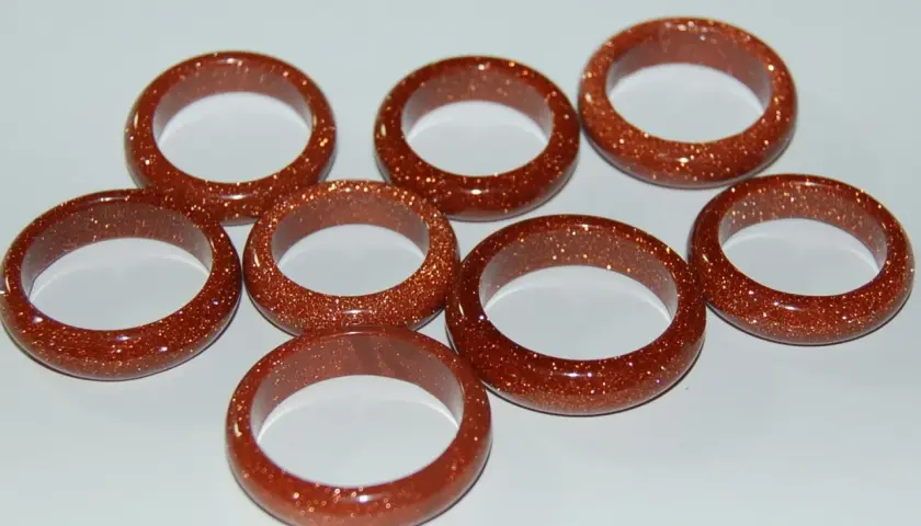 A collection of eight shimmering goldfluss stein rings, each a warm, coppery brown with flecks of gold.