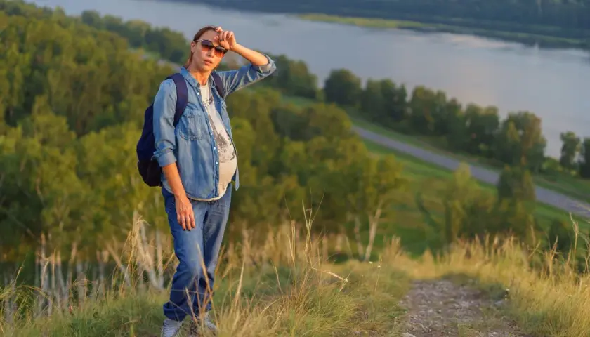 Donna in gravidanza, con zaino, su un sentiero di montagna a 1500 metri, con vista sul fiume.